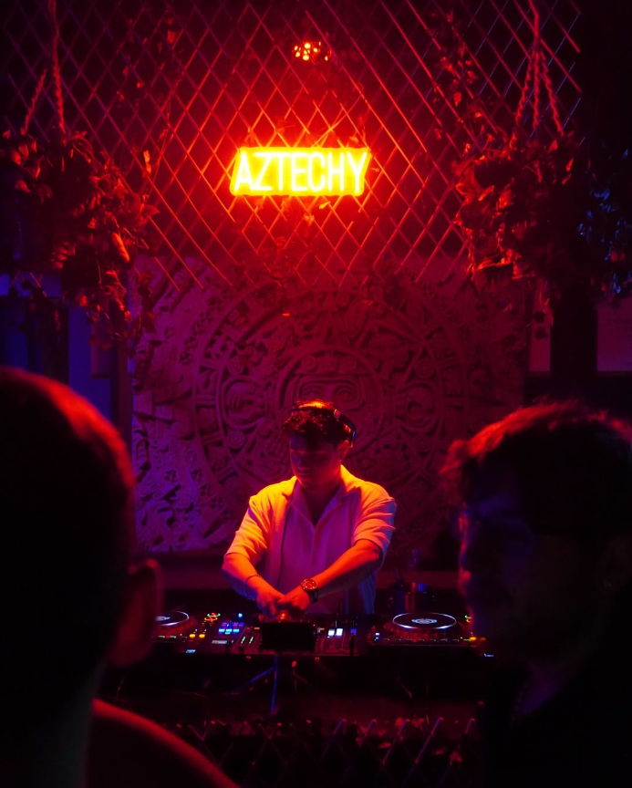 DJ performing beneath an Aztechy neon sign